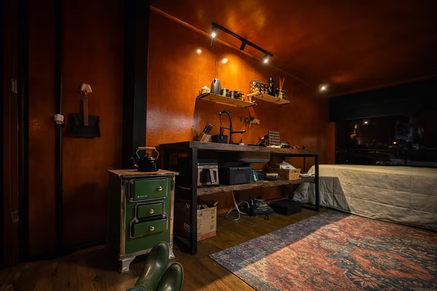 Cozinha interna da cabana à noite, com bancada rústica e fogão verde