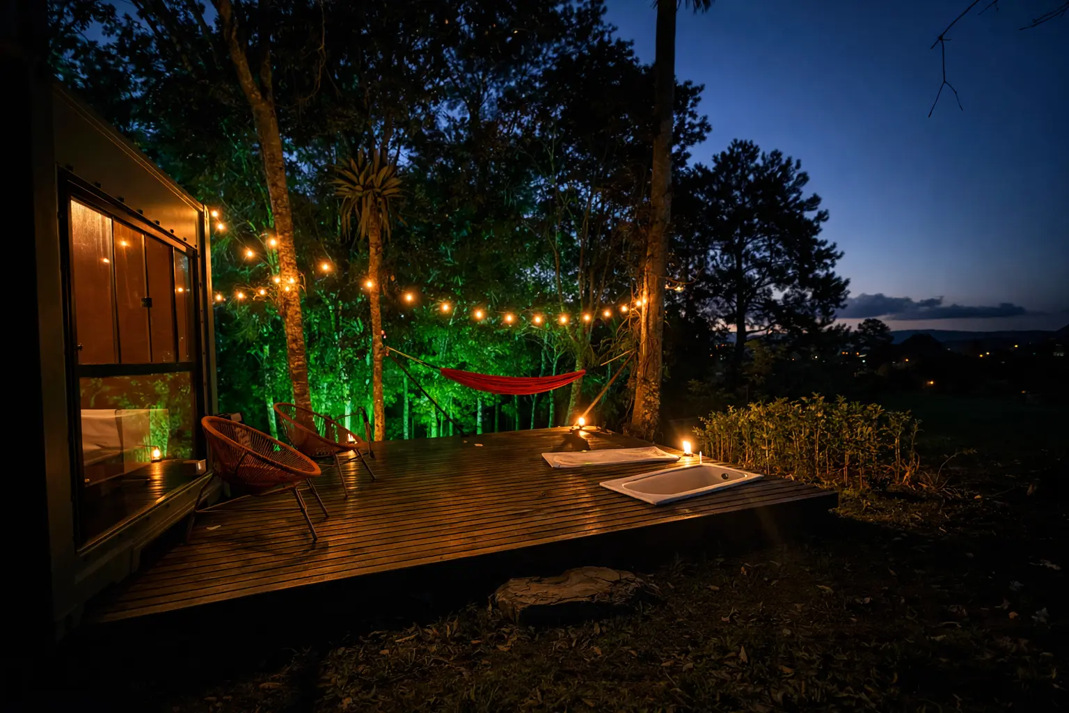 Deck ao entardecer com rede, poltronas e banheira sob luzes acolhedoras
