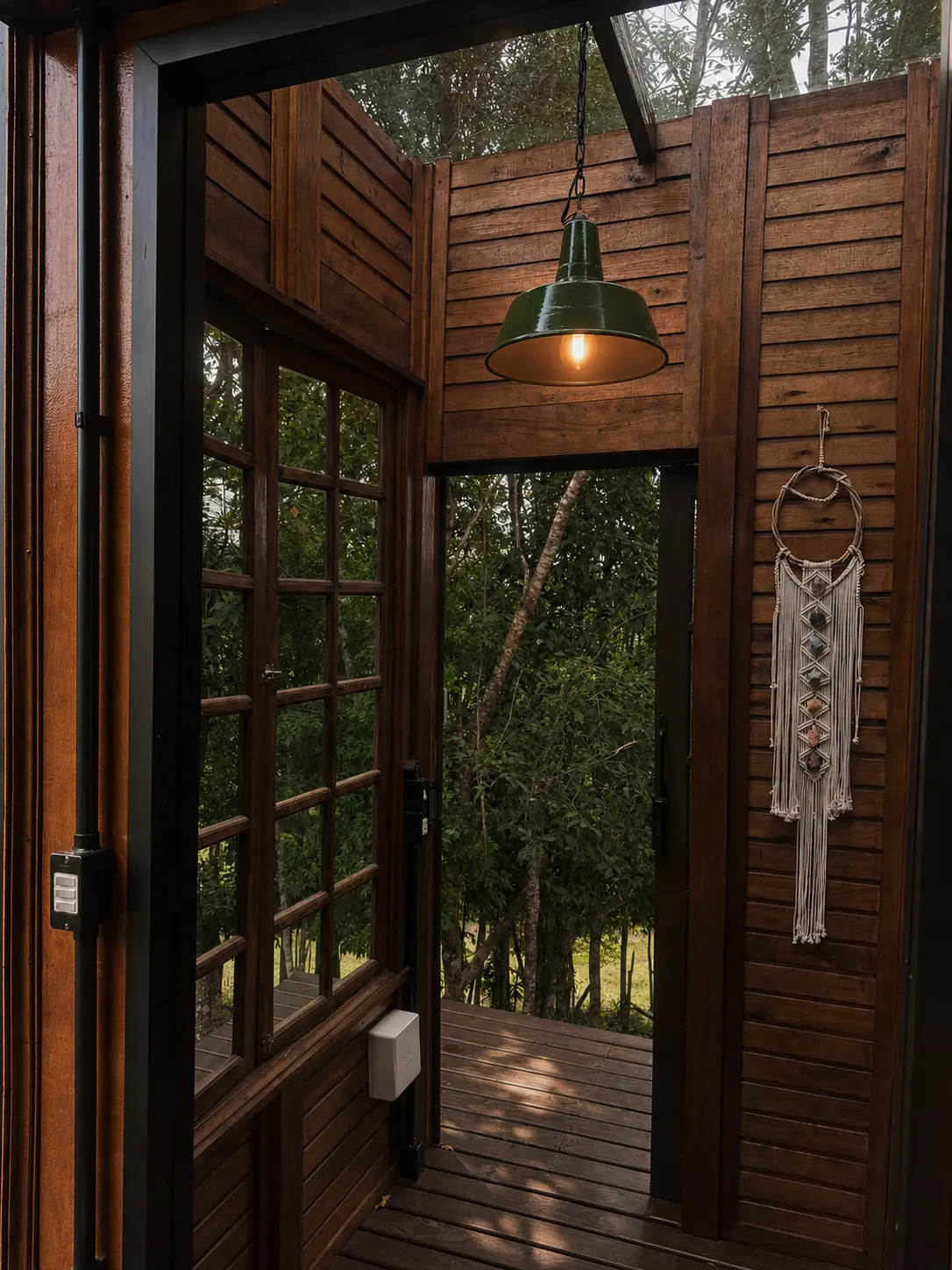 Varanda de entrada de madeira com luminária verde e vista para a mata