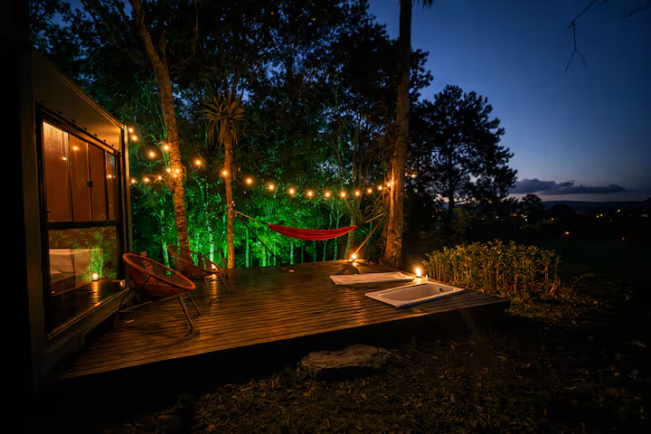 Deck iluminado com rede e luzes ao anoitecer no glamping