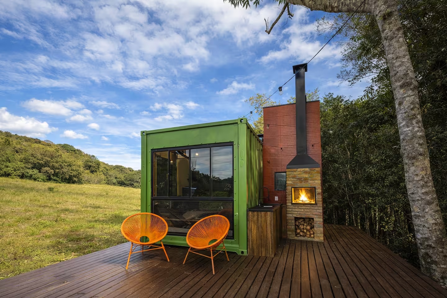 Cabana container verde de dia, com lareira externa e poltronas no deck
